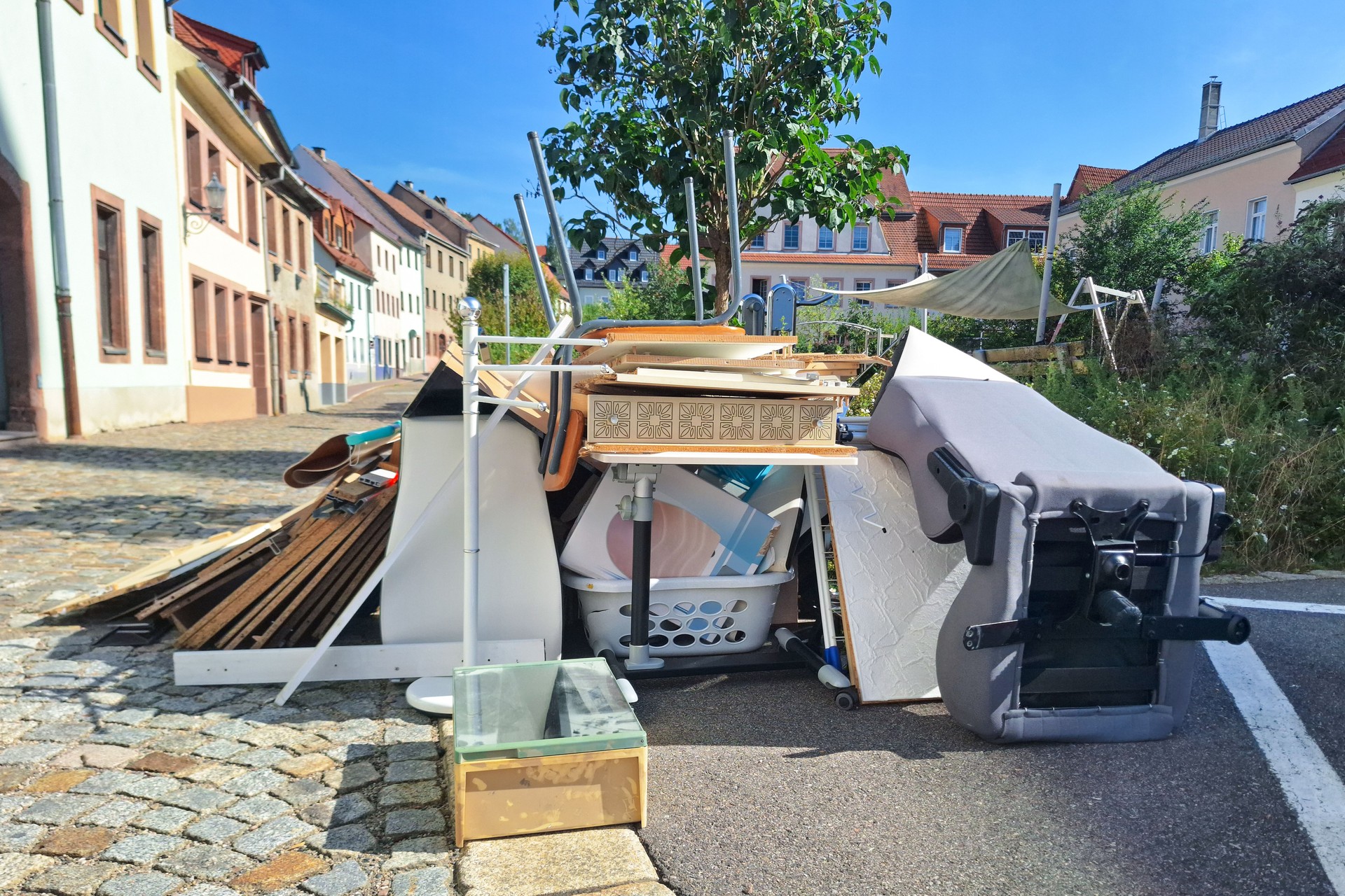 A heap of assorted discarded household items and furniture piled up on a cobblestone street, depicting a bulk waste collection day in an urban environment.